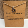 Necklace with sun pendant on a brown card with 'Good Vibes Only' text, placed on a wooden surface.