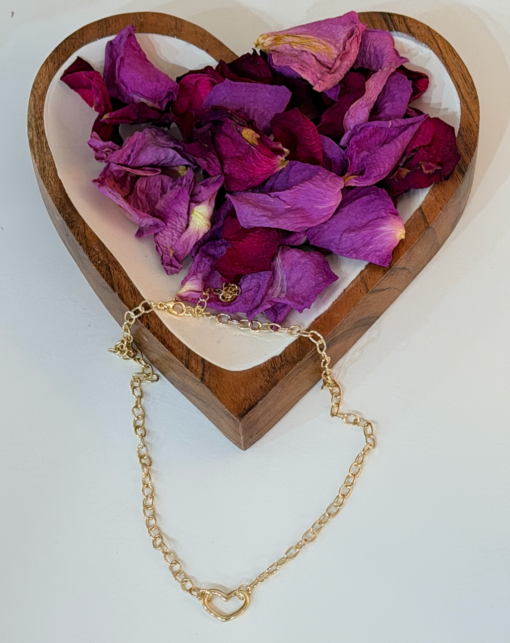 Heart-shaped dish with purple petals and a gold necklace on a white background
