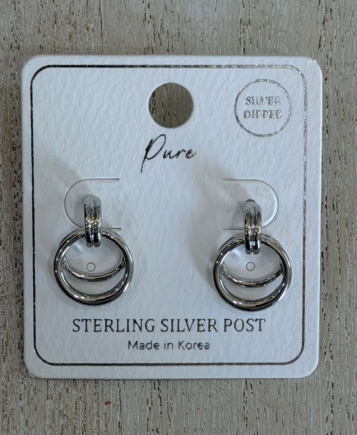 A pair of sterling silver post earrings displayed on a white branded jewelry card, placed on a light wood surface. The card reads 'Pure' and 'STERLING SILVER POST' with 'Silver Diffused' in the top right.