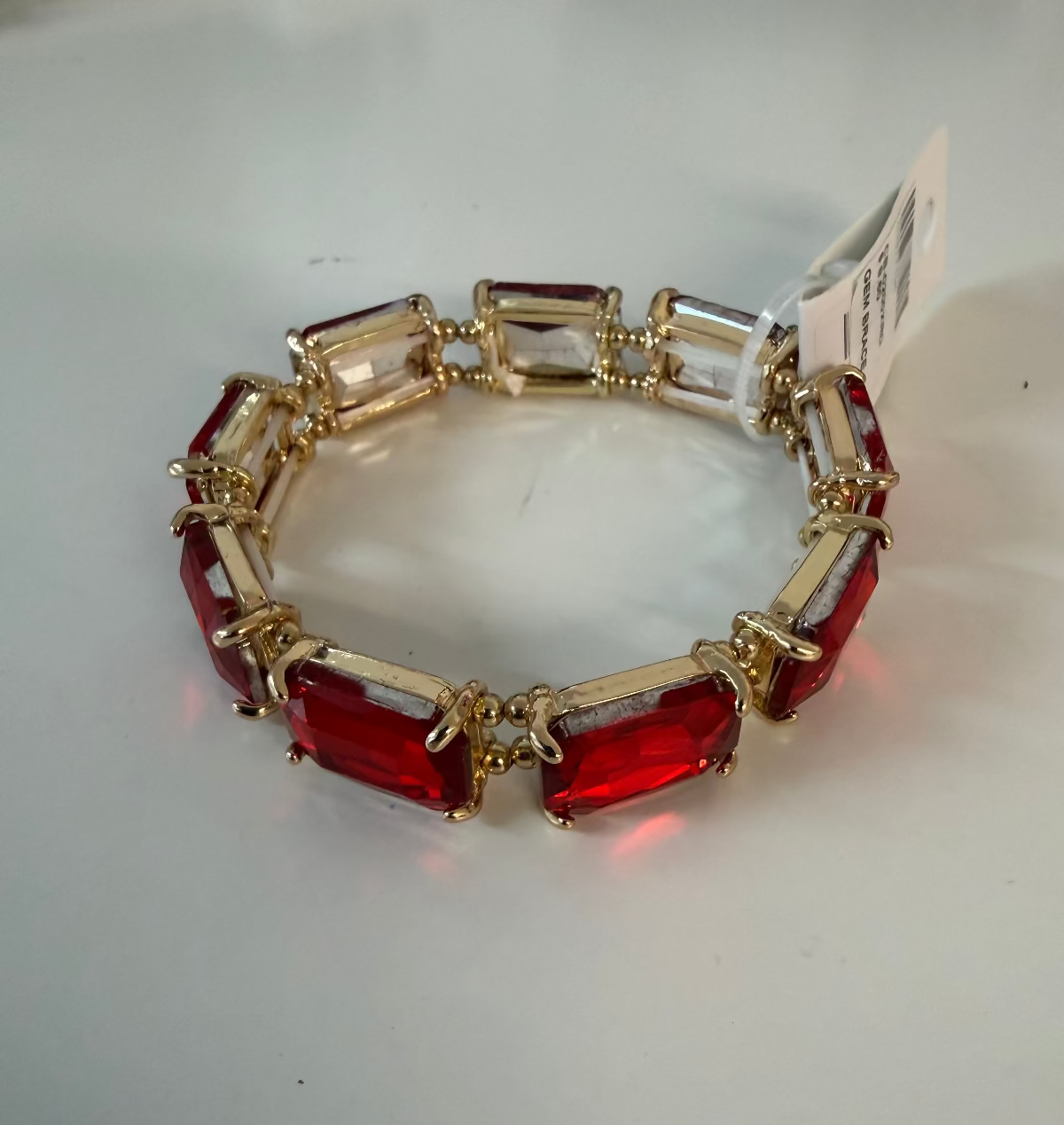 A gold-plated bracelet featuring alternating red rectangular crystal links and clear rectangular crystal links, shown on a plain light gray background with a white retail tag attached.