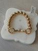 A gold beaded bracelet with a lobster clasp, displayed on a white marble stand over a gray textured surface.