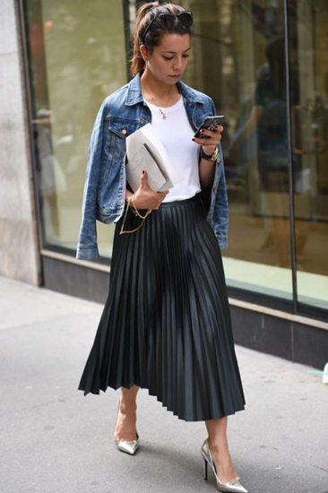 Blue denim jacket over neutral top and black pleated skirt