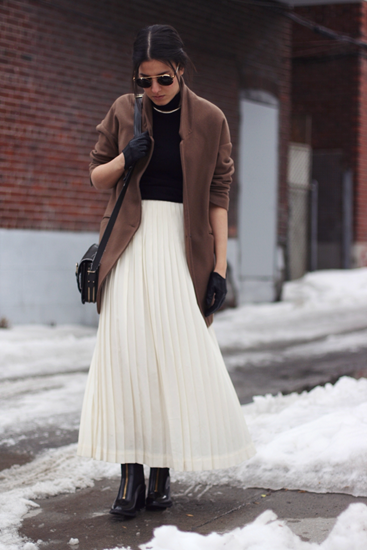 Camel coat with black turtleneck and white pleated skirt